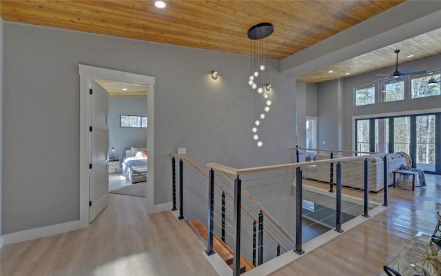 hallway with light wood-style flooring, wooden ceiling, an upstairs landing, and baseboards