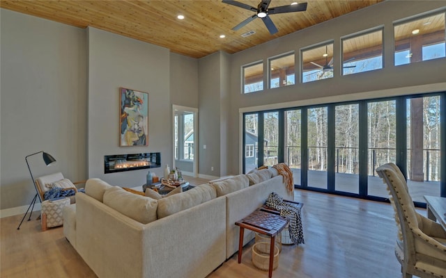 living room featuring a glass covered fireplace, wood ceiling, baseboards, and wood finished floors