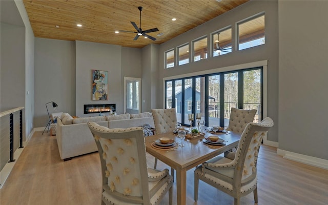 dining space with light wood finished floors, a glass covered fireplace, wood ceiling, and recessed lighting