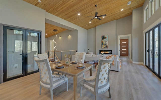 dining area featuring a glass covered fireplace, wood ceiling, light wood-style flooring, french doors, and high vaulted ceiling