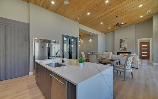 kitchen with a sink, an island with sink, modern cabinets, high vaulted ceiling, and a warm lit fireplace