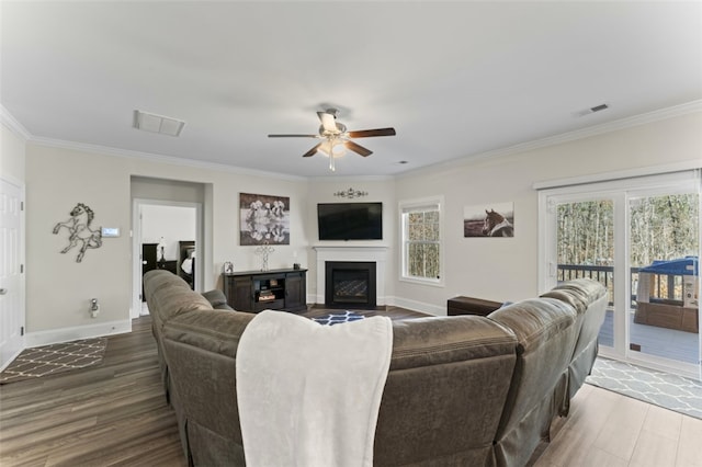 living room featuring a fireplace with flush hearth, crown molding, baseboards, and wood finished floors