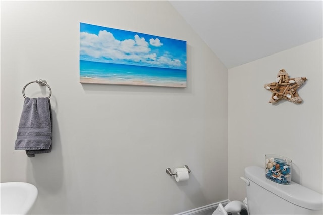 half bathroom featuring vaulted ceiling, toilet, and baseboards