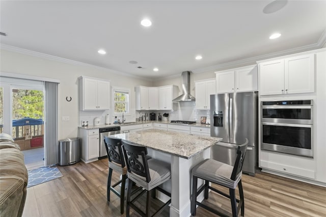 kitchen with stainless steel appliances, wall chimney range hood, a kitchen island, and white cabinetry