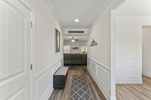 corridor featuring a wainscoted wall, a decorative wall, crown molding, and wood finished floors