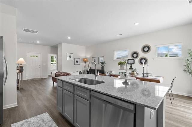 kitchen featuring a center island with sink, open floor plan, stainless steel appliances, gray cabinetry, and a sink