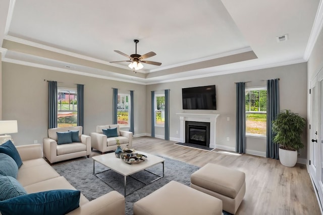 living area featuring visible vents, baseboards, a tray ceiling, light wood finished floors, and a glass covered fireplace