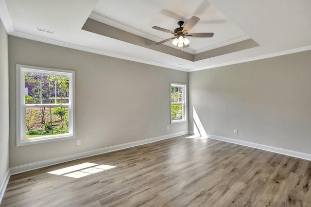 spare room featuring light wood finished floors, a raised ceiling, visible vents, and baseboards