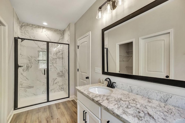 full bathroom featuring a marble finish shower, wood finished floors, a walk in closet, vanity, and recessed lighting