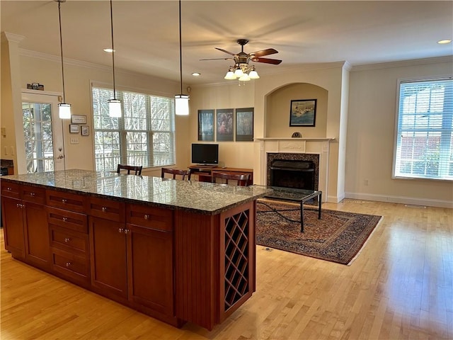 kitchen with crown molding, a fireplace, a center island, dark stone counters, and pendant lighting