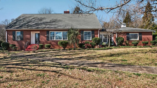 view of front of home featuring a front yard, brick siding, and a chimney