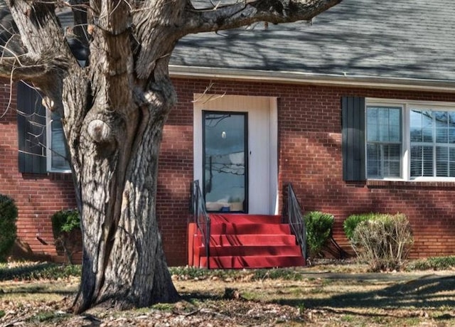 view of exterior entry featuring brick siding and roof with shingles