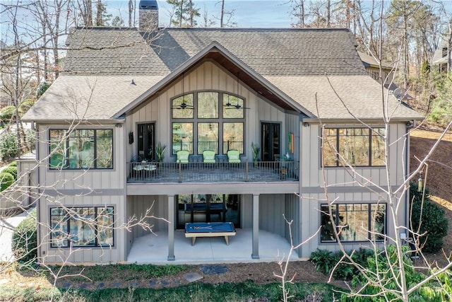 back of house with a shingled roof, a chimney, board and batten siding, and a patio