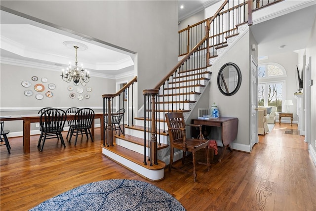 stairway featuring wood finished floors, baseboards, ornamental molding, a raised ceiling, and an inviting chandelier