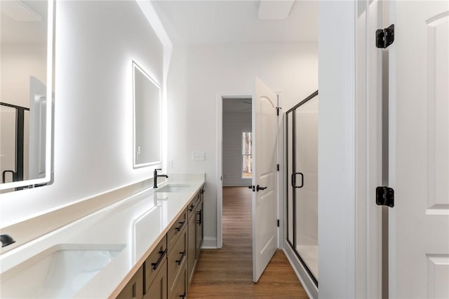 full bathroom featuring double vanity, wood finished floors, a stall shower, and a sink