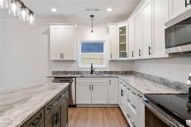 kitchen with white cabinets, glass insert cabinets, appliances with stainless steel finishes, decorative light fixtures, and a sink