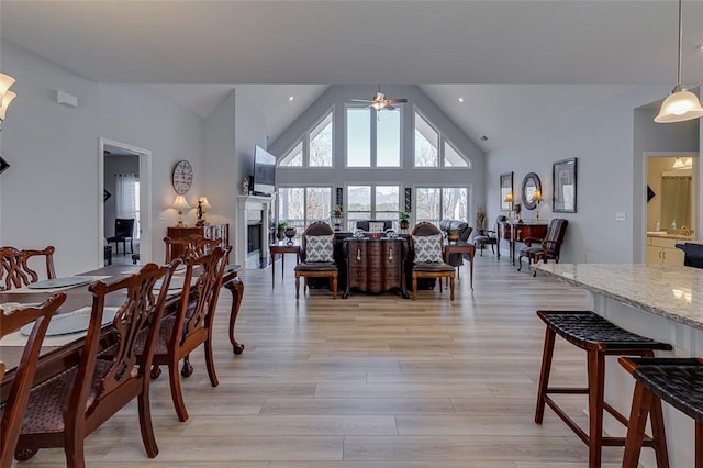 dining room with a ceiling fan, light wood-style floors, a fireplace, high vaulted ceiling, and recessed lighting