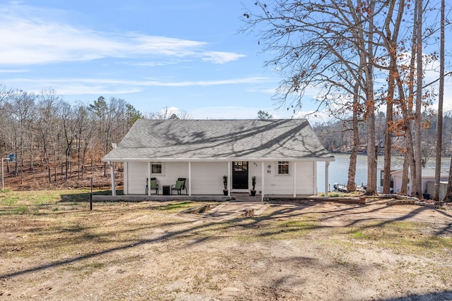 back of property with a water view, covered porch, and a lawn