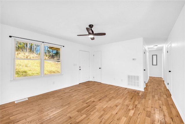 spare room with light wood finished floors, a ceiling fan, visible vents, and baseboards