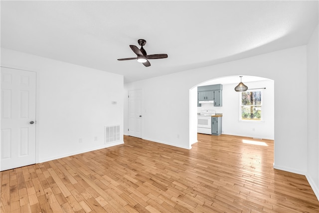 unfurnished living room with arched walkways, ceiling fan, light wood-style flooring, visible vents, and baseboards