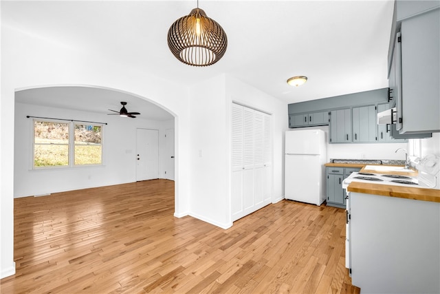 kitchen with arched walkways, freestanding refrigerator, hanging light fixtures, light wood-style floors, and wooden counters