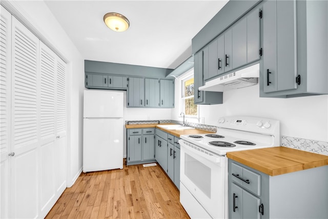 kitchen with white appliances, light wood finished floors, butcher block counters, under cabinet range hood, and a sink