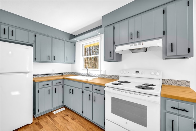 kitchen featuring white appliances, light wood-style floors, wood counters, under cabinet range hood, and a sink