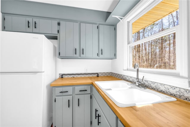 kitchen with gray cabinets, freestanding refrigerator, butcher block counters, and a sink