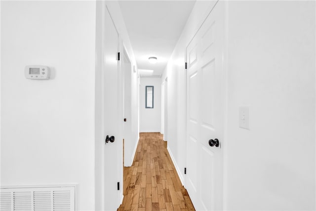 hallway featuring light wood-style floors, visible vents, and baseboards