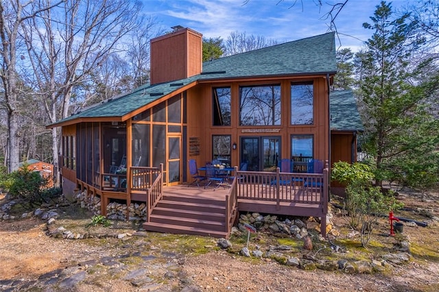 rear view of property with a sunroom, roof with shingles, a chimney, and a wooden deck