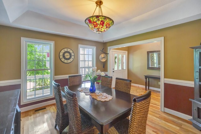 dining area with light wood-style flooring, visible vents, a tray ceiling, and baseboards