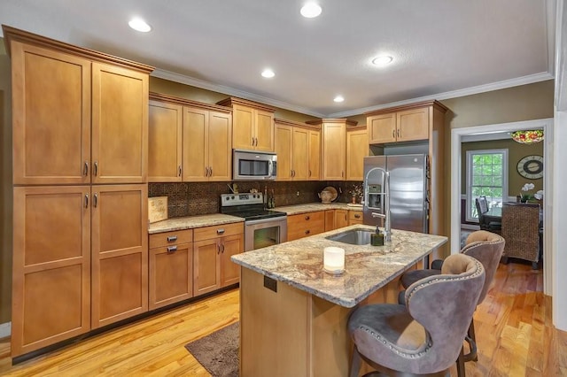 kitchen featuring a breakfast bar, a sink, appliances with stainless steel finishes, light stone countertops, and a center island with sink