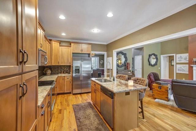 kitchen with a sink, open floor plan, appliances with stainless steel finishes, an island with sink, and a kitchen bar