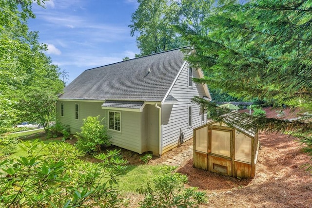 back of house featuring roof with shingles, an outbuilding, and an exterior structure