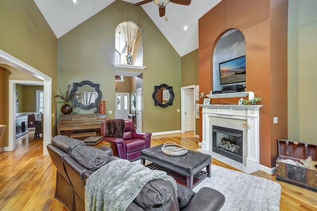 living area with high vaulted ceiling, a wealth of natural light, a fireplace with flush hearth, and light wood-style flooring