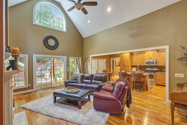 living area featuring high vaulted ceiling, light wood-type flooring, and a ceiling fan