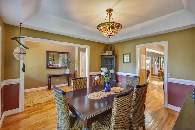 dining space featuring light wood-type flooring, baseboards, and a tray ceiling