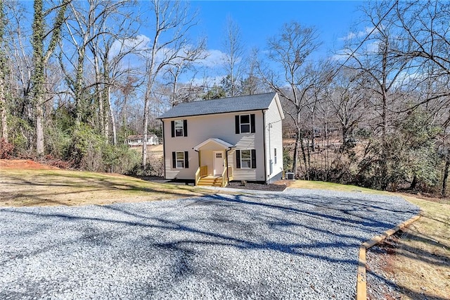 colonial inspired home with entry steps, a front lawn, and gravel driveway