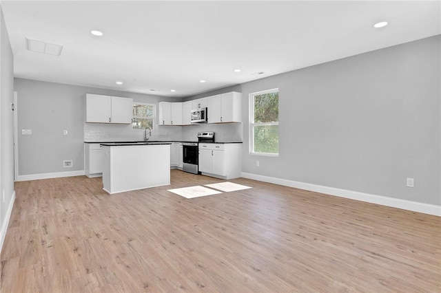 kitchen featuring stainless steel appliances, a sink, baseboards, open floor plan, and decorative backsplash