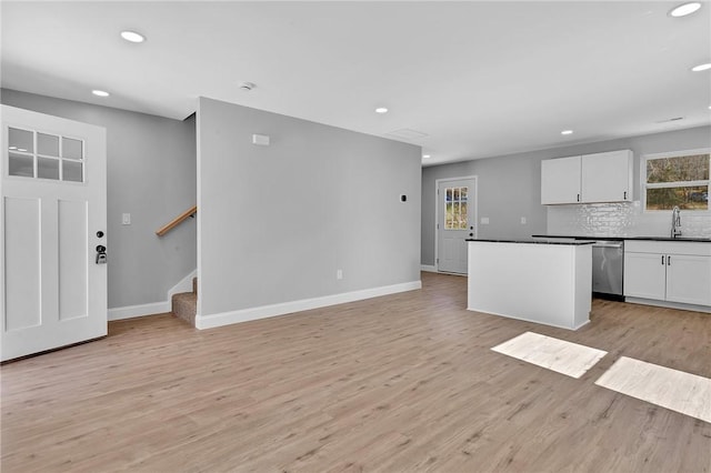 kitchen featuring baseboards, white cabinets, stainless steel dishwasher, backsplash, and light wood finished floors