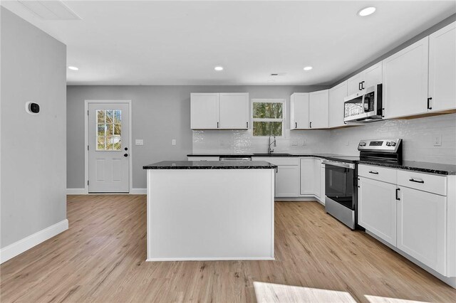 kitchen with light wood finished floors, a kitchen island, appliances with stainless steel finishes, a sink, and backsplash