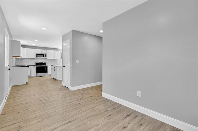 kitchen featuring light wood finished floors, baseboards, appliances with stainless steel finishes, and backsplash