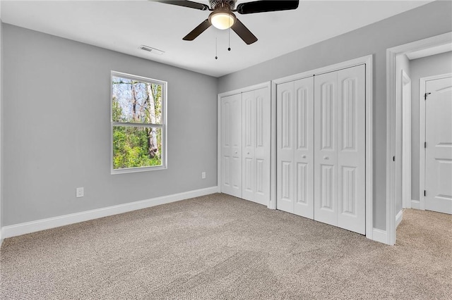 unfurnished bedroom with baseboards, visible vents, carpet flooring, and two closets