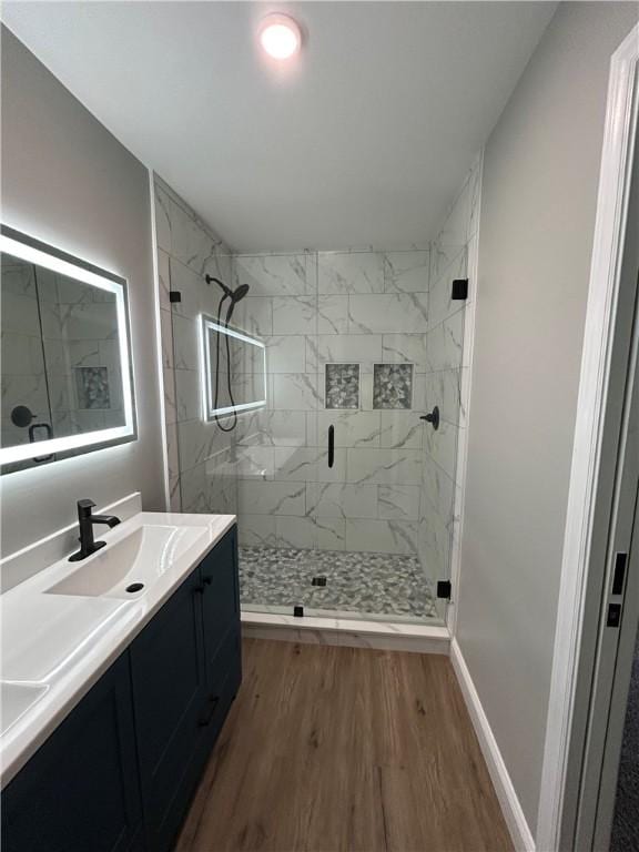 bathroom with a marble finish shower, double vanity, a sink, wood finished floors, and baseboards