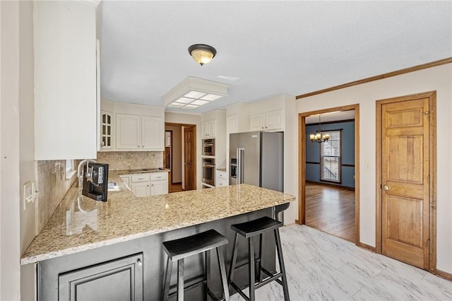 kitchen featuring a peninsula, a sink, white cabinetry, decorative backsplash, and light stone countertops