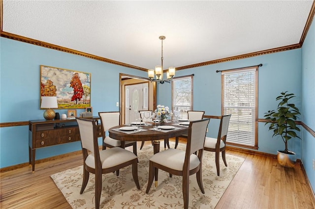 dining room featuring light wood-style flooring, ornamental molding, a textured ceiling, a chandelier, and baseboards