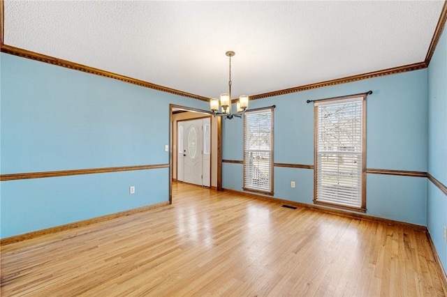 spare room with a notable chandelier, light wood finished floors, visible vents, ornamental molding, and baseboards