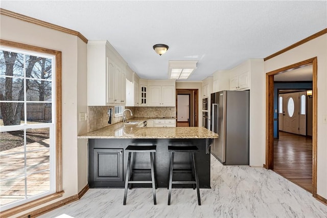 kitchen with a breakfast bar, marble finish floor, high end fridge, a sink, and a peninsula