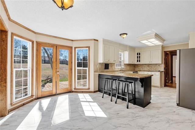 kitchen featuring a peninsula, a breakfast bar, marble finish floor, ornamental molding, and glass insert cabinets