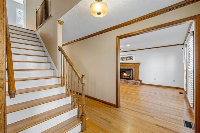 stairway featuring visible vents, ornamental molding, wood finished floors, a textured ceiling, and a brick fireplace